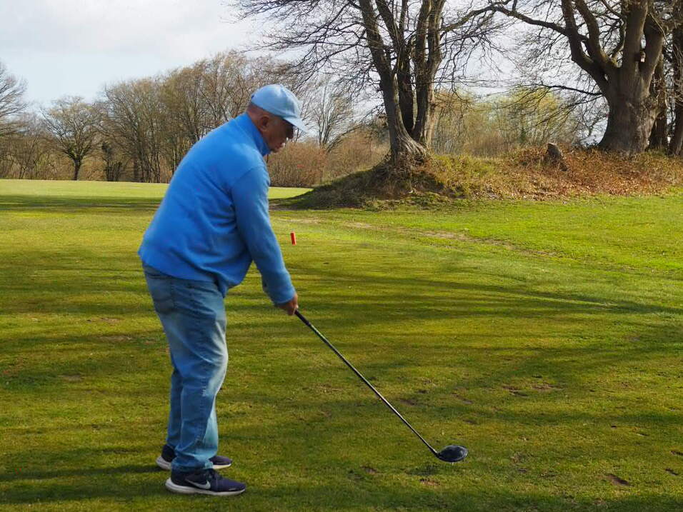 Mann in blauer Jacke bereitet sich auf den Abschlag mit einem Golfschl&auml;ger auf einer gr&uuml;nen Golfbahn vor.