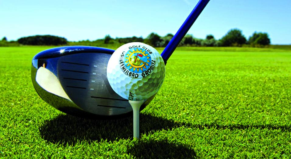 Nahaufnahme eines Golfballs auf einem Tee neben einem Golfschläger auf einem gepflegten Golfplatz.