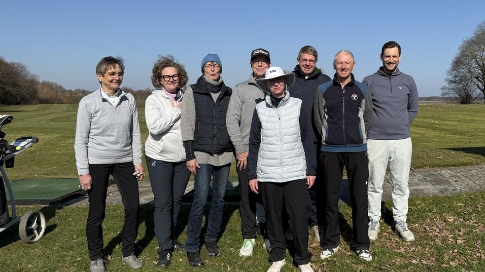 Gruppenshot von acht Golfspielern auf einem Abschlagplatz bei klarem Himmel und gr&uuml;nem Rasen.