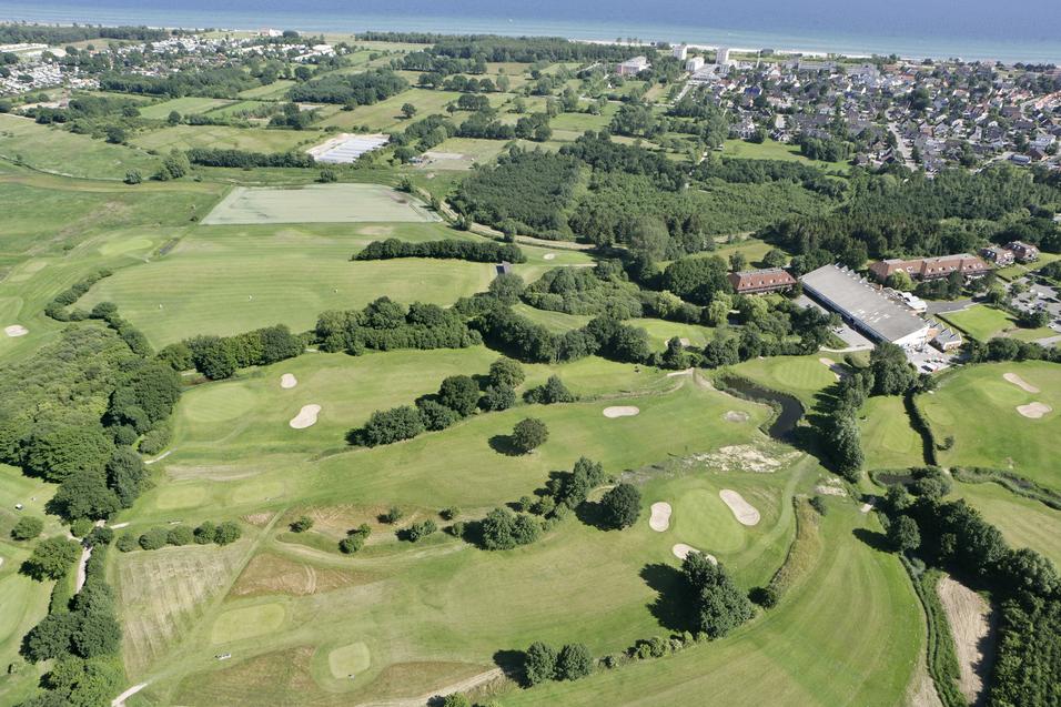 Luftaufnahme einer weitläufigen Golfplatzlandschaft mit Grünflächen, Bunkern und angrenzenden Wohngebieten.