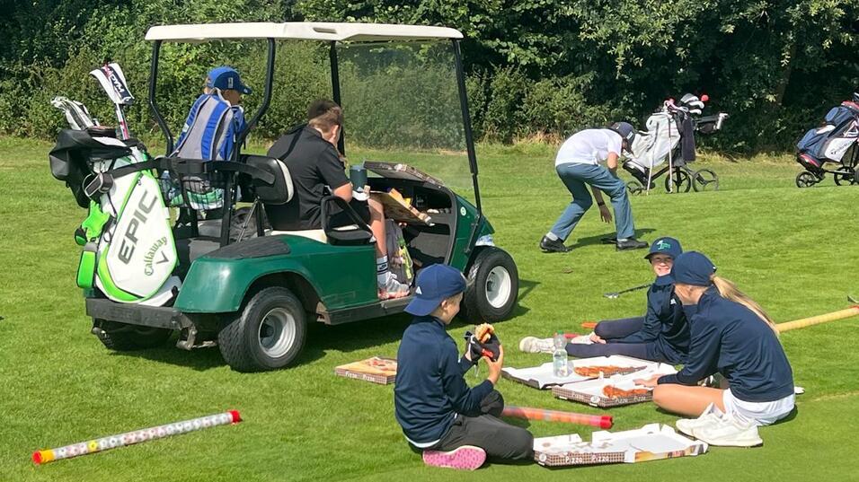 Gruppierung von Jugendlichen, die auf dem Golfplatz trainieren, mit einem Golfwagen im Hintergrund und Golfausr&uuml;stung.
